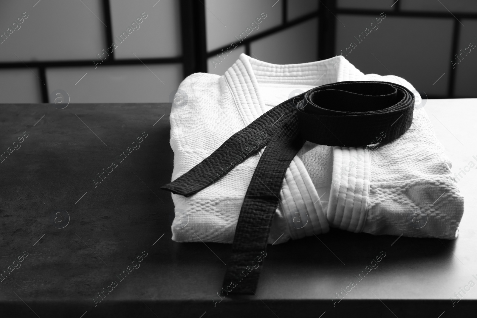 Photo of Martial arts uniform with black belt on grey stone table indoors