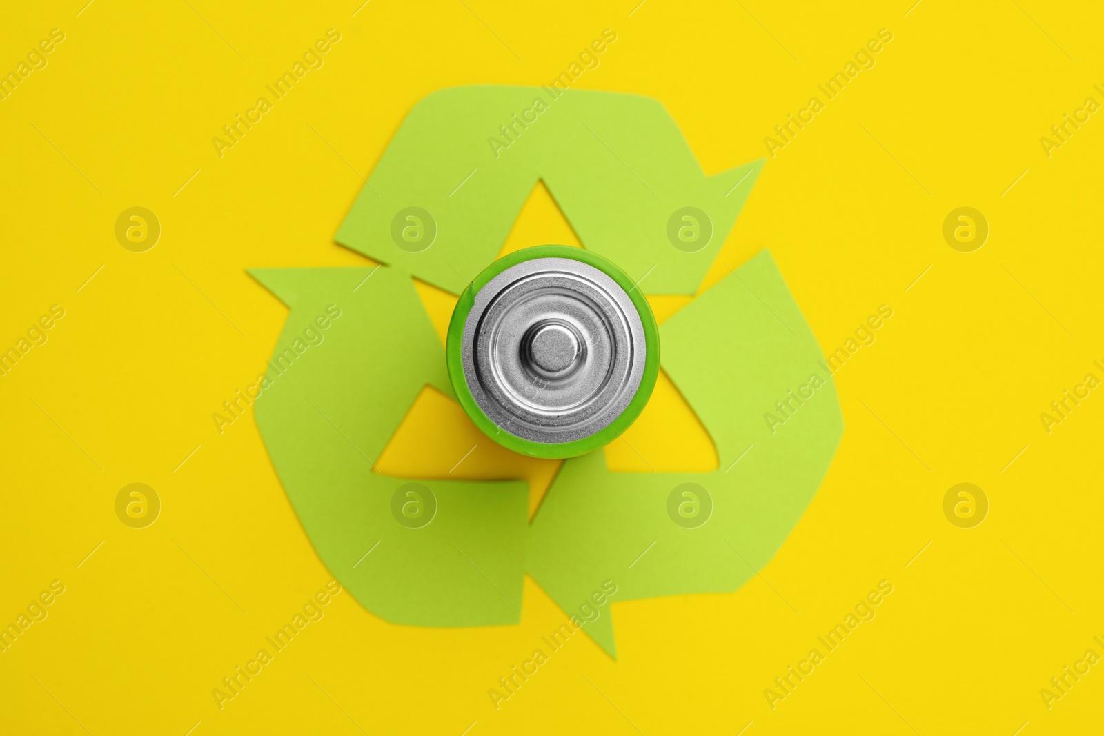 Photo of Used battery and recycling symbol on yellow background, top view