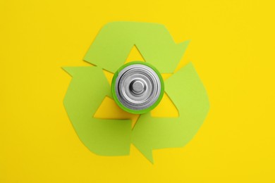 Photo of Used battery and recycling symbol on yellow background, top view