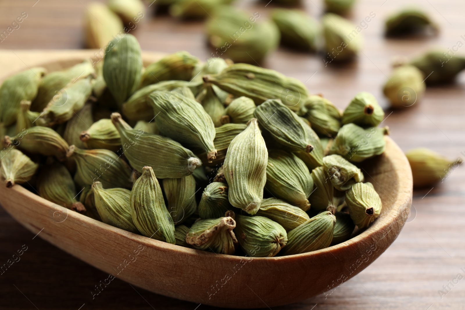 Photo of Spoon with dry cardamom pods on wooden table, closeup