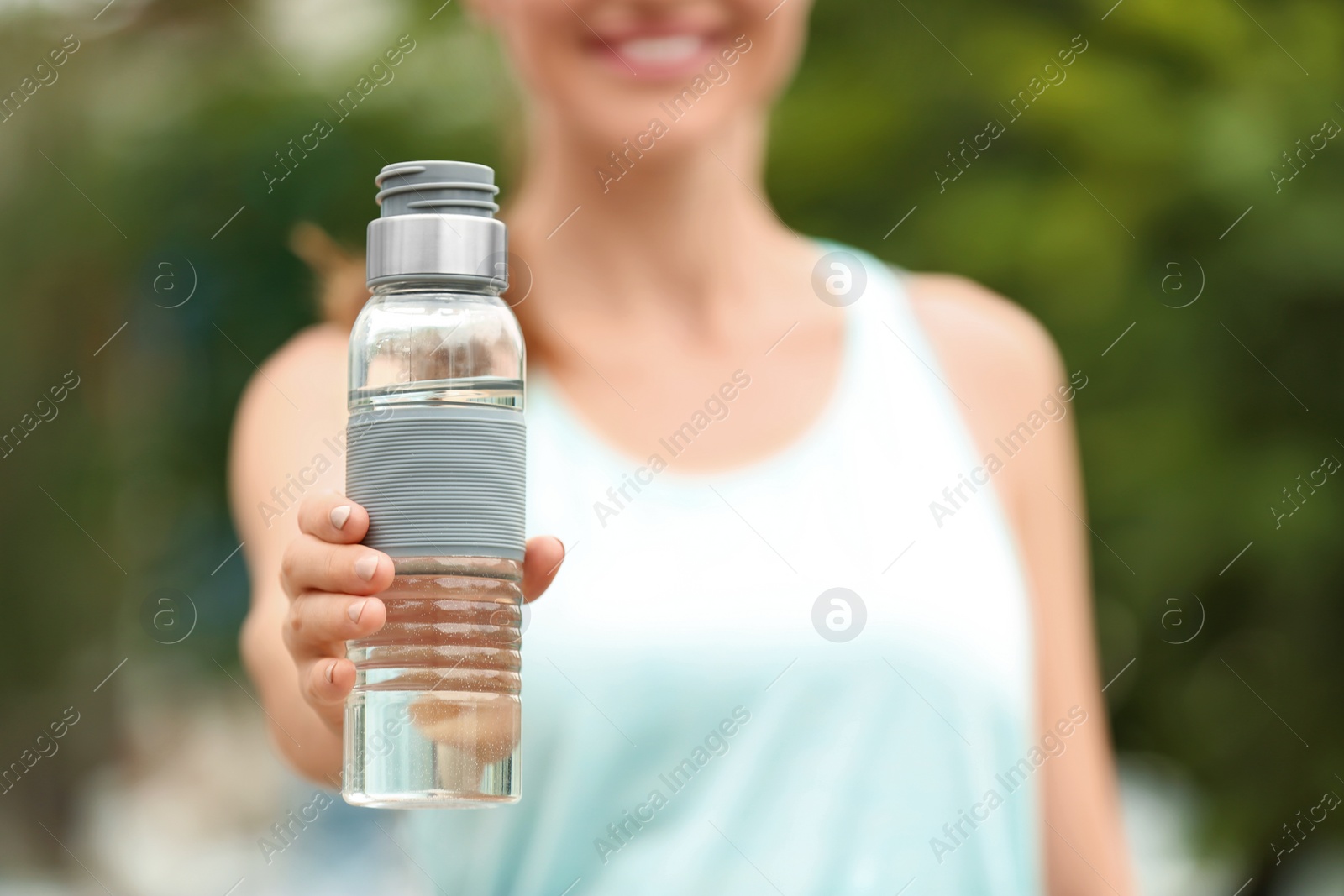 Photo of Young woman with bottle of water outdoors, closeup. Refreshing drink