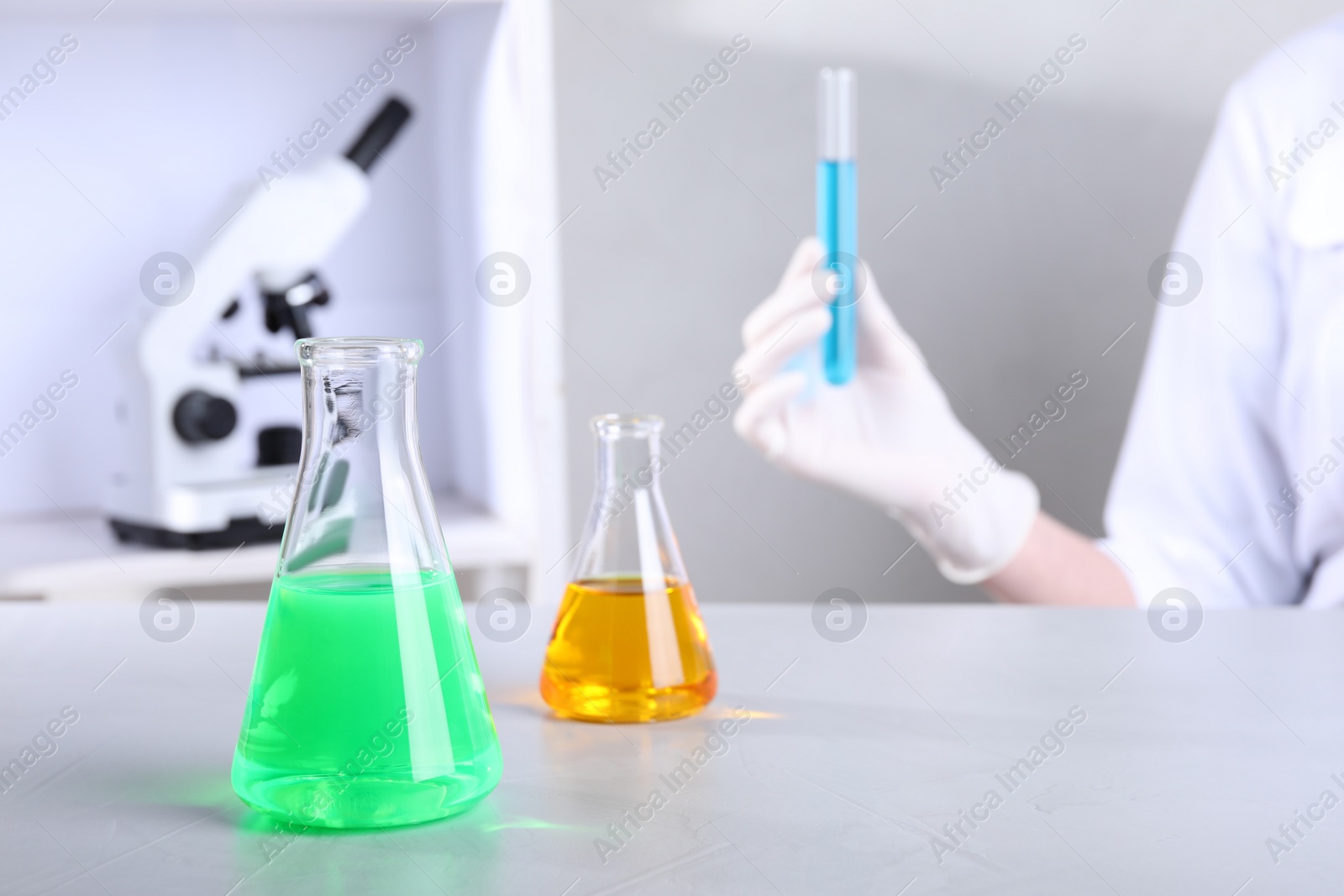 Photo of Glassware with samples on table and assistant in chemistry laboratory