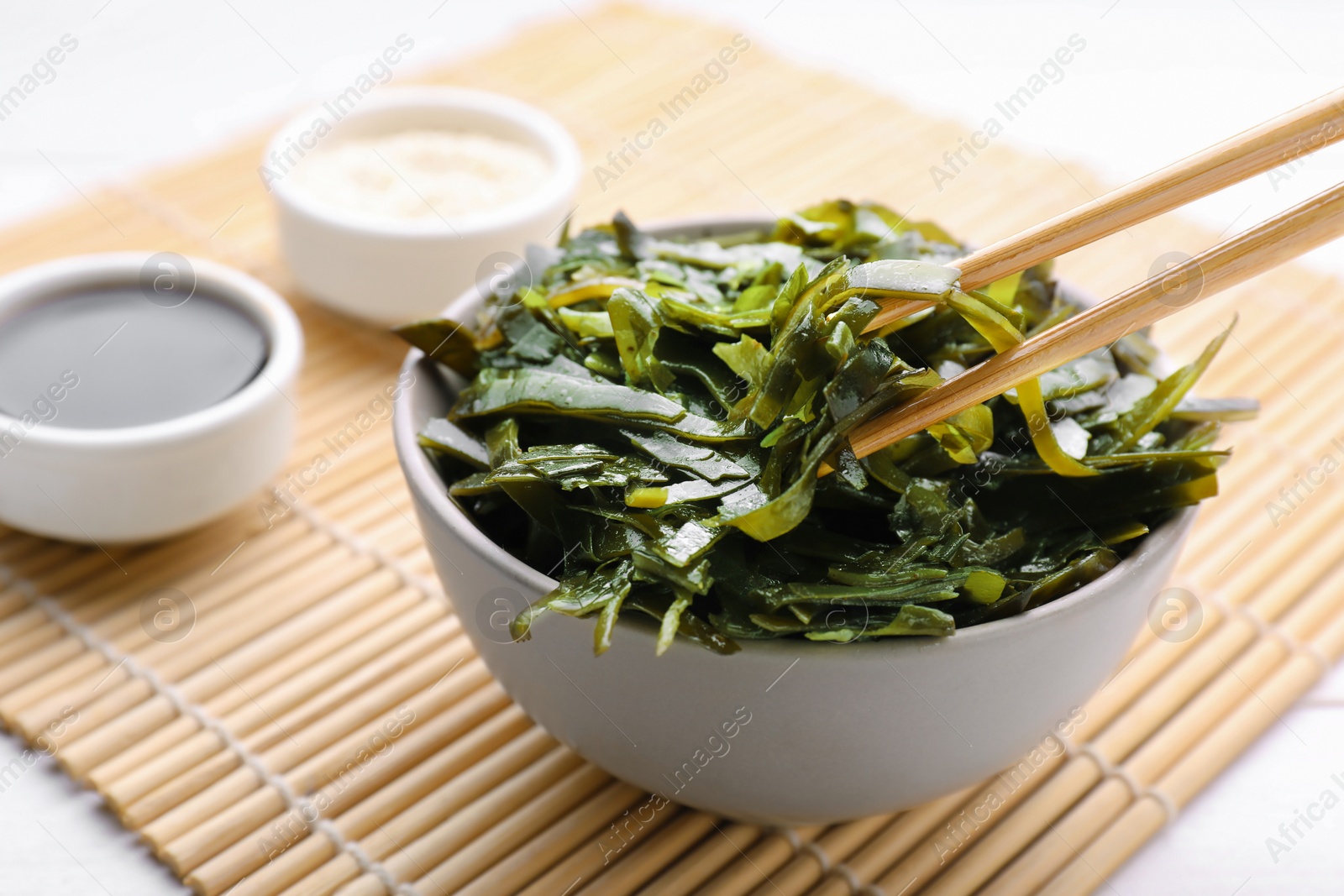 Photo of Fresh laminaria (kelp) seaweed in bowl and chopsticks on white table