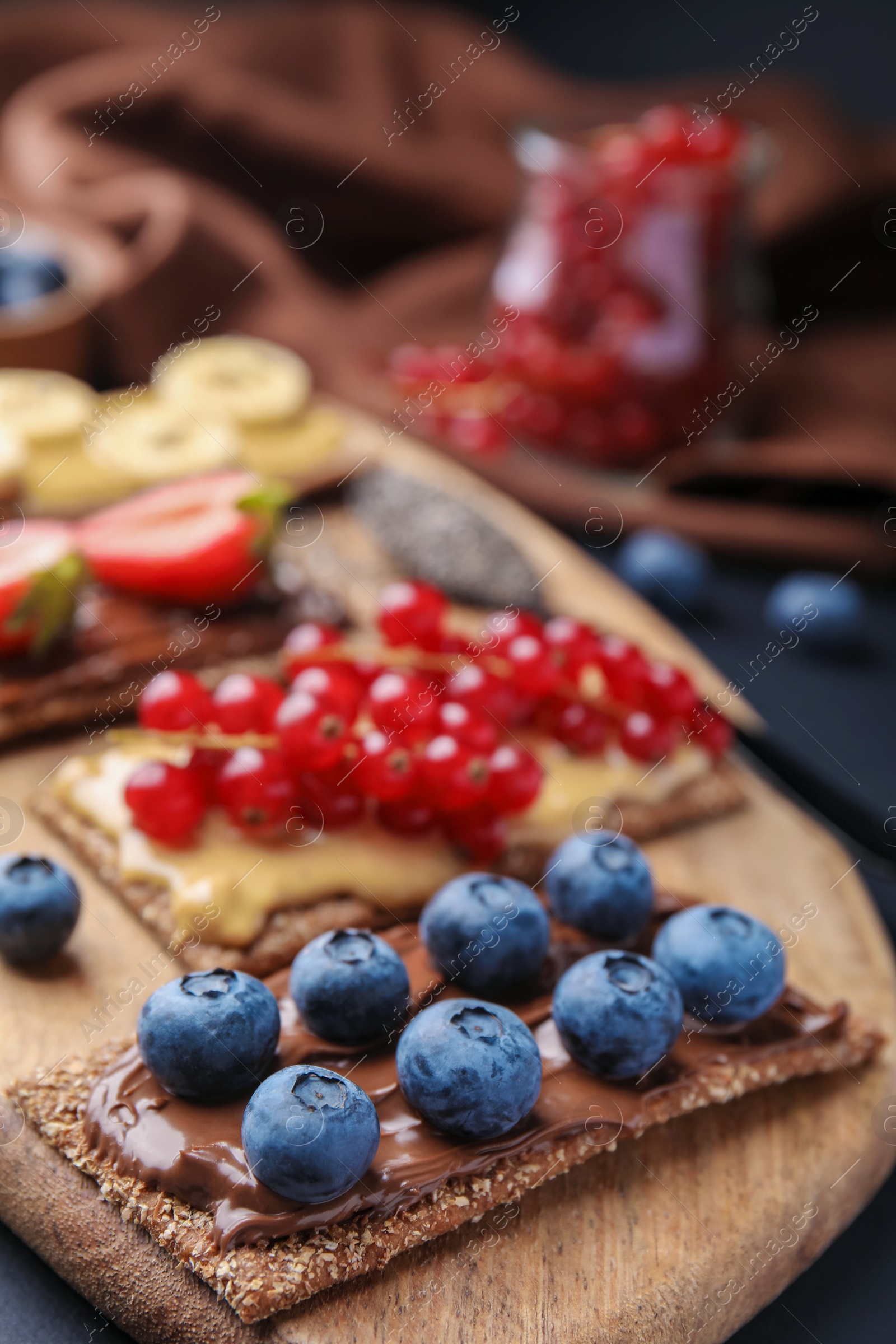 Photo of Fresh crunchy rye crispbreads with different toppings on wooden board, closeup