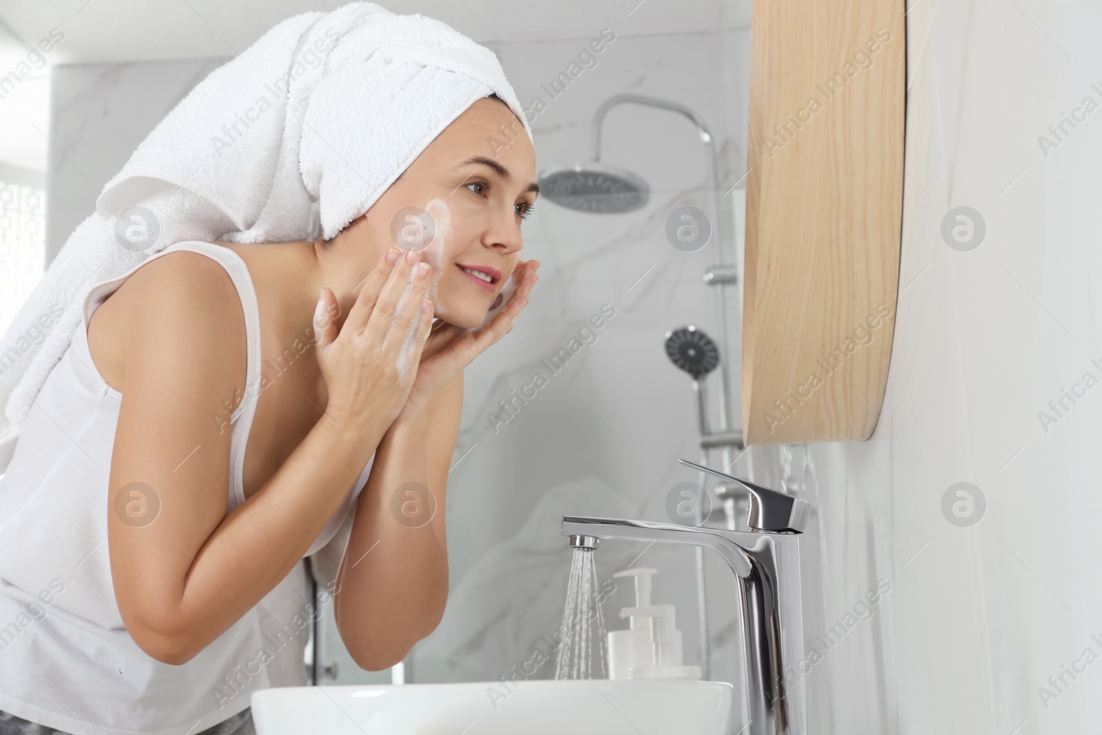 Photo of Happy mature woman washing face in bathroom