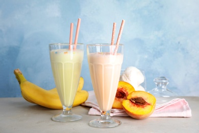 Delicious milk shakes and ingredients on table against color background