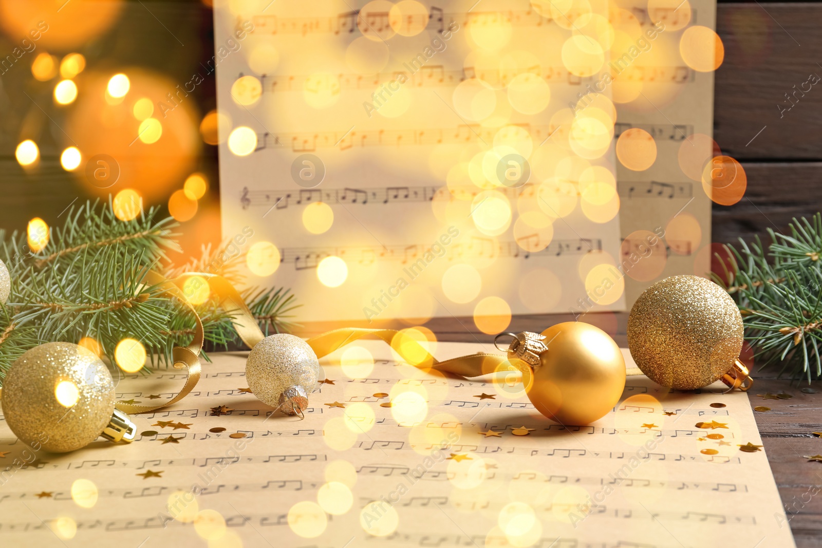 Image of Christmas and New Year music. Fir tree branch, festive balls and music sheets on wooden background, bokeh effect