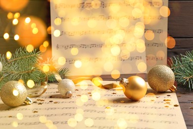 Christmas and New Year music. Fir tree branch, festive balls and music sheets on wooden background, bokeh effect