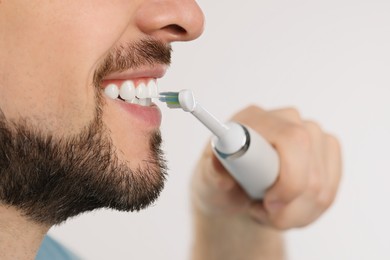 Man brushing his teeth with electric toothbrush on white background, closeup