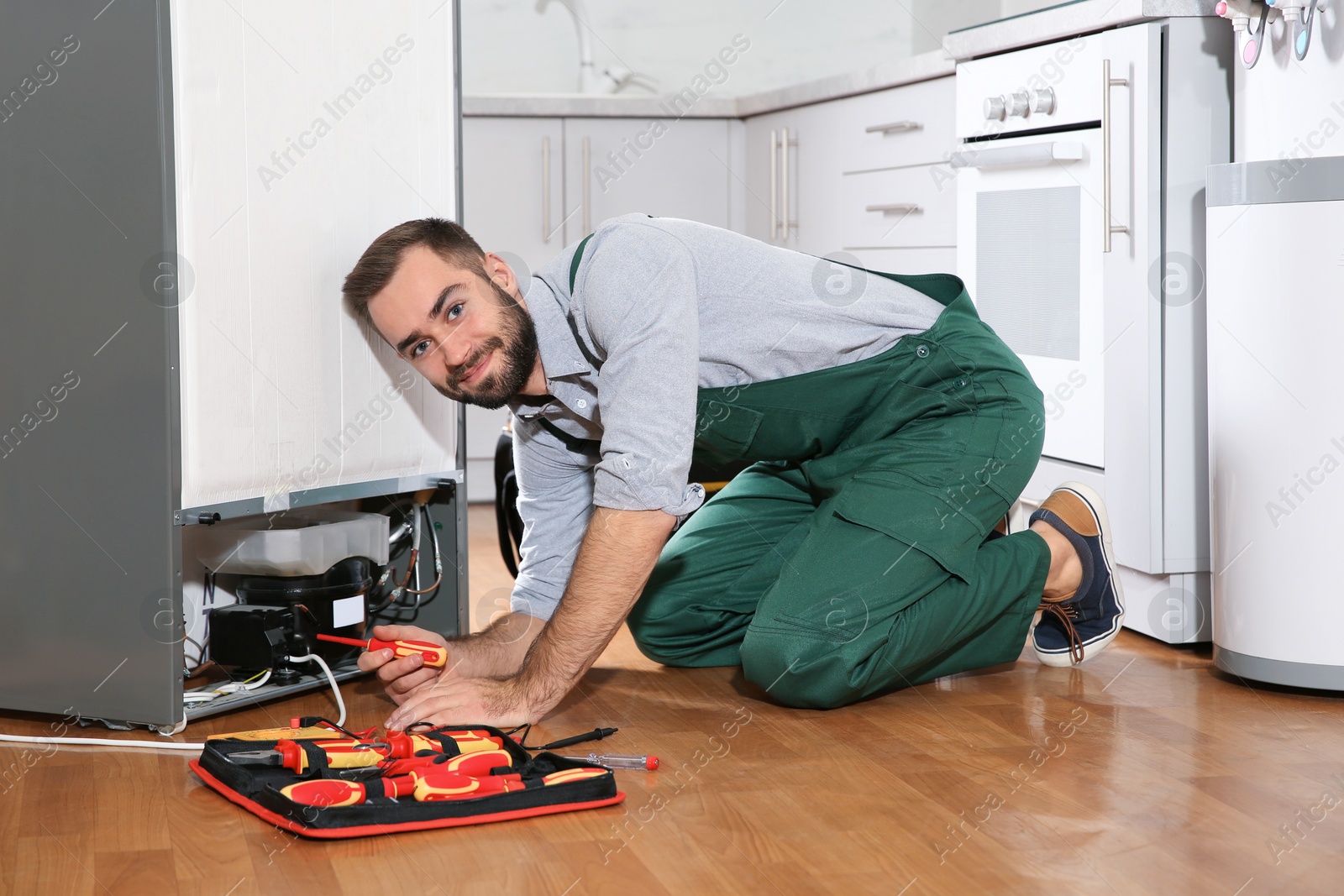 Photo of Male technician in uniform repairing refrigerator indoors