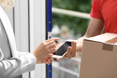 Woman using smartphone app to confirm receipt of parcel from courier near door