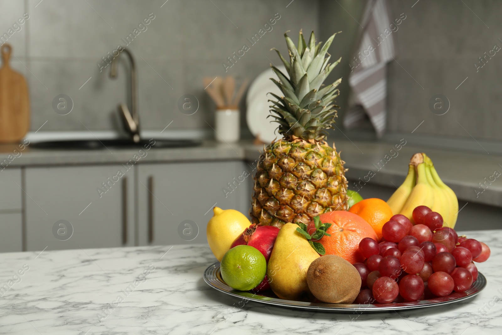 Photo of Plate with different ripe fruits on white marble table in kitchen. Space for text