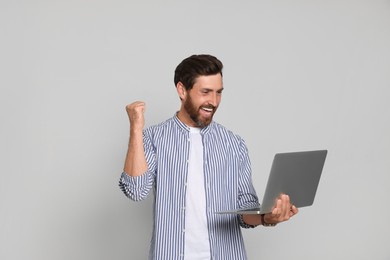 Photo of Happy handsome man with laptop on light background