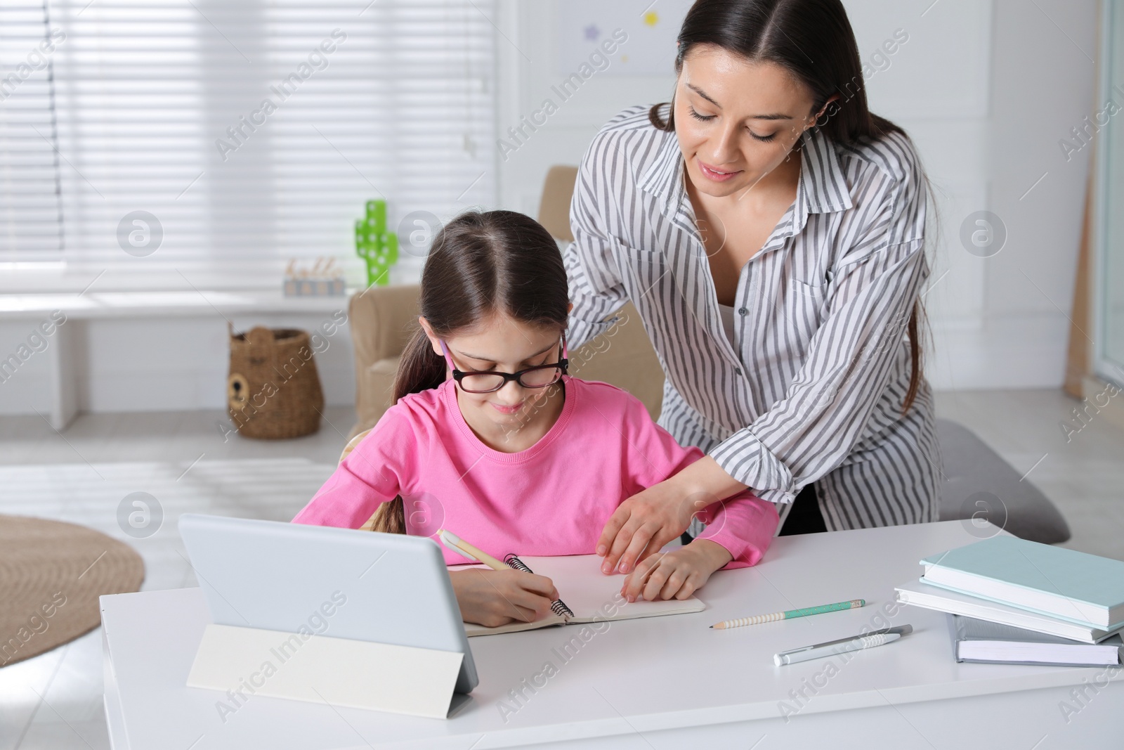 Photo of Mother helping her daughter doing homework with tablet at home