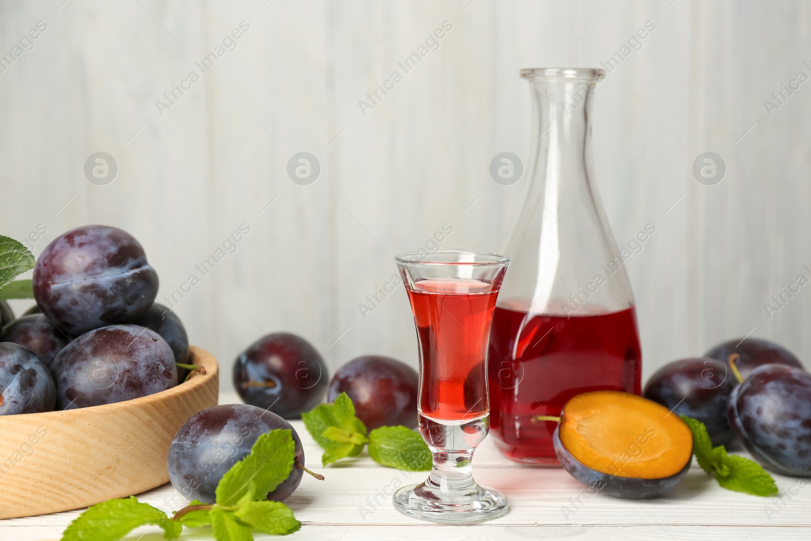 Photo of Delicious plum liquor, ripe fruits and mint on white wooden table. Homemade strong alcoholic beverage