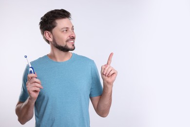 Photo of Happy man holding electric toothbrush on white background. Space for text