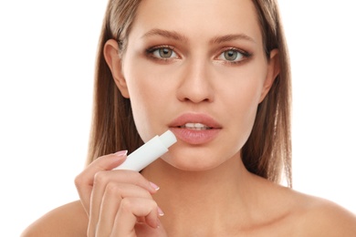 Photo of Young woman with cold sore applying lip balm against white background