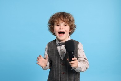 Photo of Cute little boy with microphone singing on light blue background