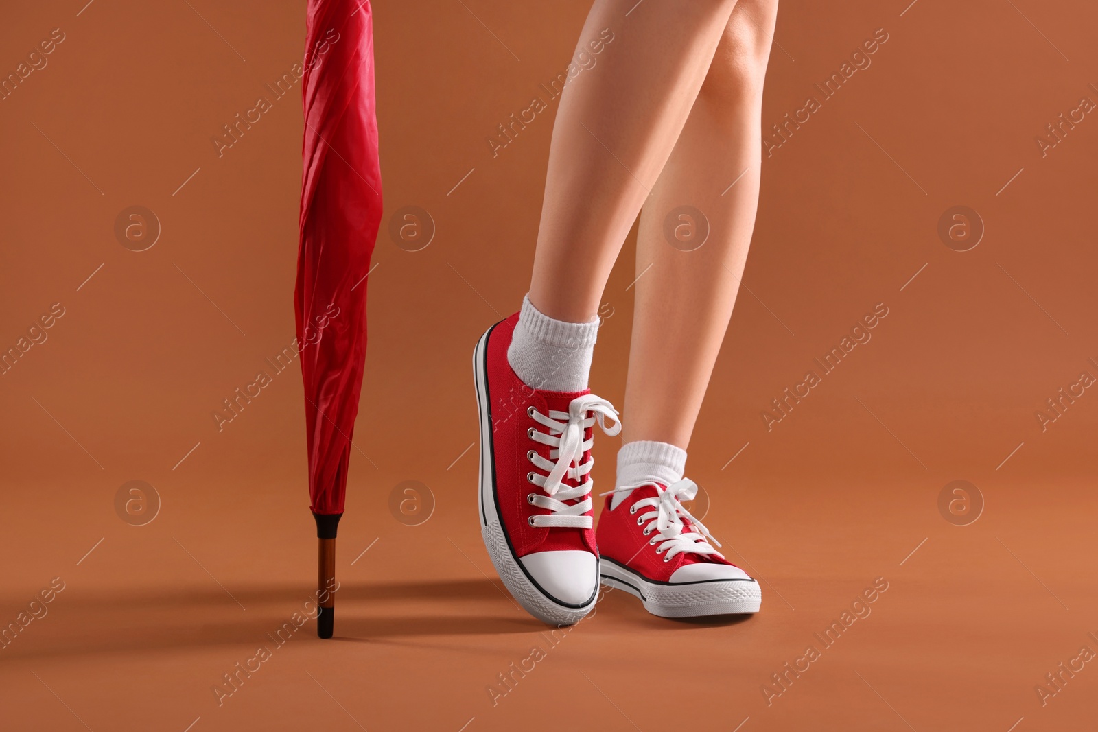 Photo of Woman in red classic old school sneakers and umbrella on brown background, closeup