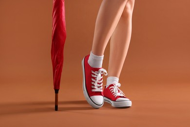 Photo of Woman in red classic old school sneakers and umbrella on brown background, closeup