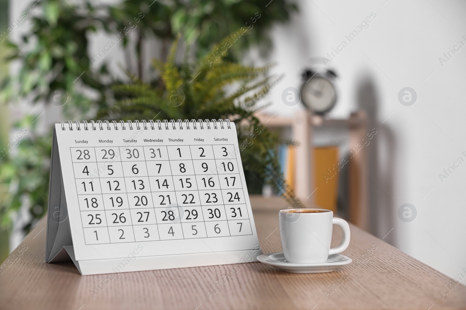 Photo of Calendar and cup of coffee on wooden table against blurred background