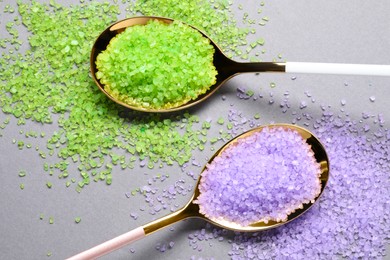 Photo of Spoons with lilac and light green sea salt on grey table, closeup
