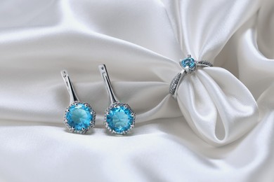Photo of Beautiful ring and earrings with light blue gemstones on white fabric. Luxury jewelry