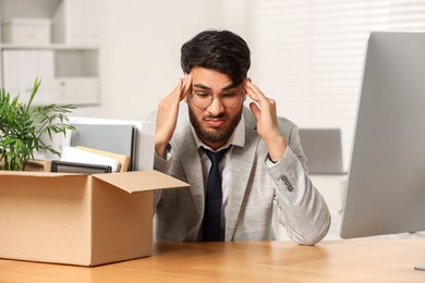 Photo of Unemployment problem. Frustrated man with box of personal belongings at desk in office