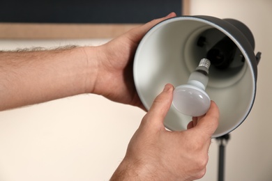 Man changing light bulb in desk lamp indoors, closeup