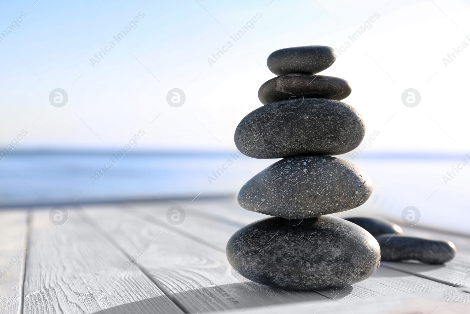 Photo of Stack of dark stones on wooden deck near sea, space for text. Zen concept