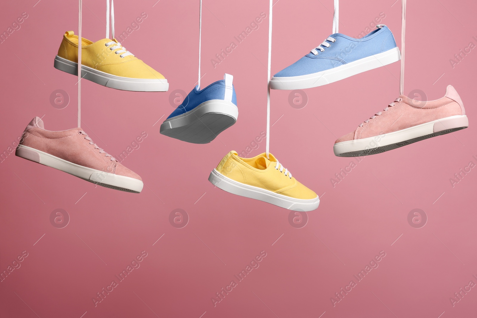 Photo of Bright stylish shoes hanging against color background