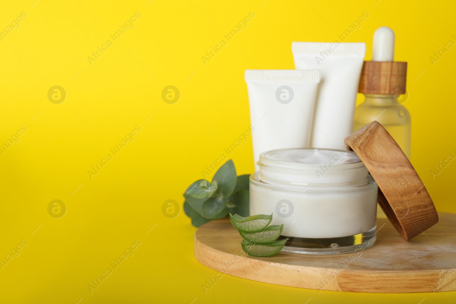 Photo of Body cream and other cosmetics, aloe with eucalyptus on yellow background. Space for text