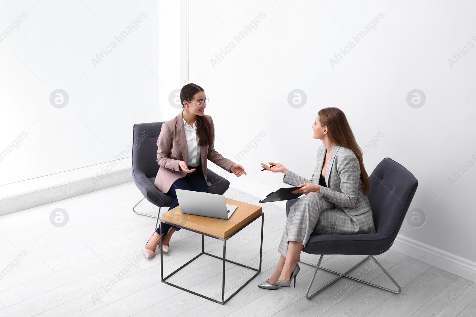 Photo of Young businesswomen sitting in armchairs at table indoors