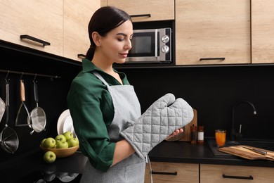 Photo of Woman wearing apron and oven glove in kitchen