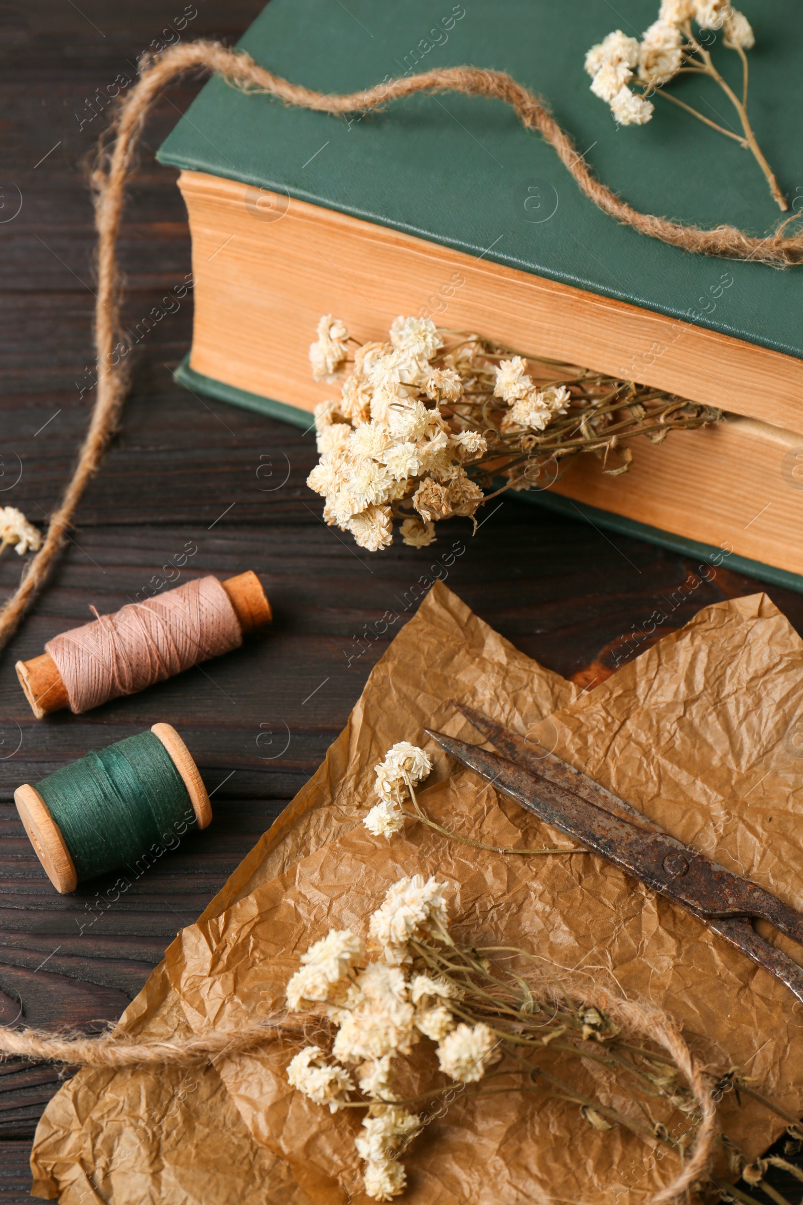 Photo of Flat lay composition of book with flowers as bookmark and scissors on wooden table