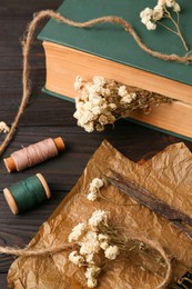 Photo of Flat lay composition of book with flowers as bookmark and scissors on wooden table