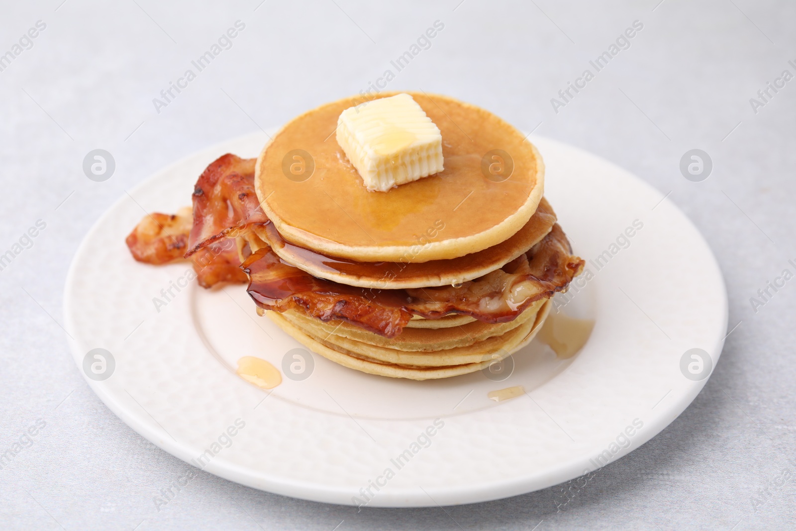 Photo of Delicious pancakes with bacon, butter and honey on light table, closeup