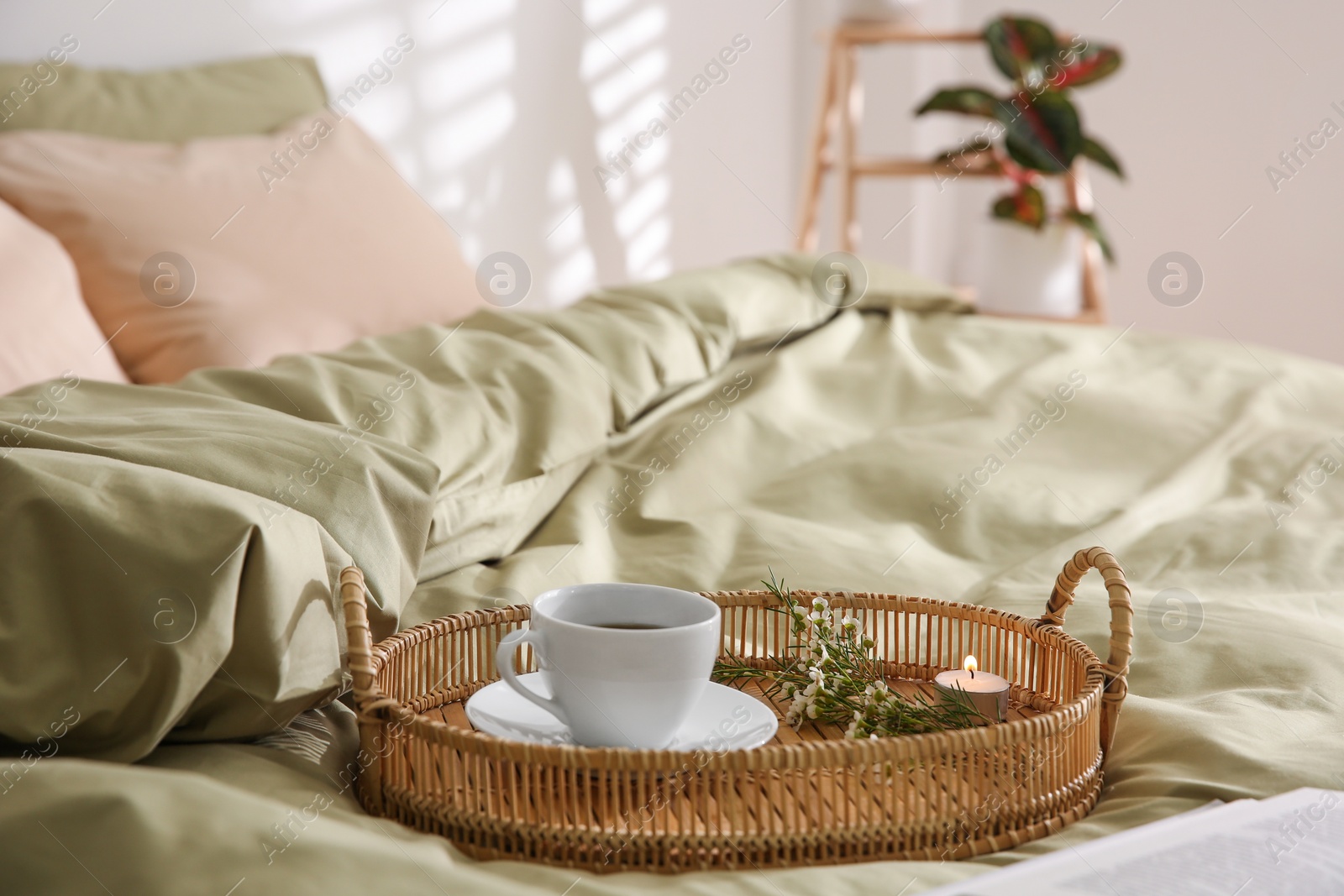 Photo of Tray with cup of coffee, candle and flowers on soft olive blanket indoors