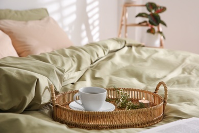 Photo of Tray with cup of coffee, candle and flowers on soft olive blanket indoors