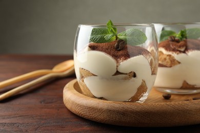 Delicious tiramisu in glasses, mint leaves and coffee beans on wooden table, closeup. Space for text