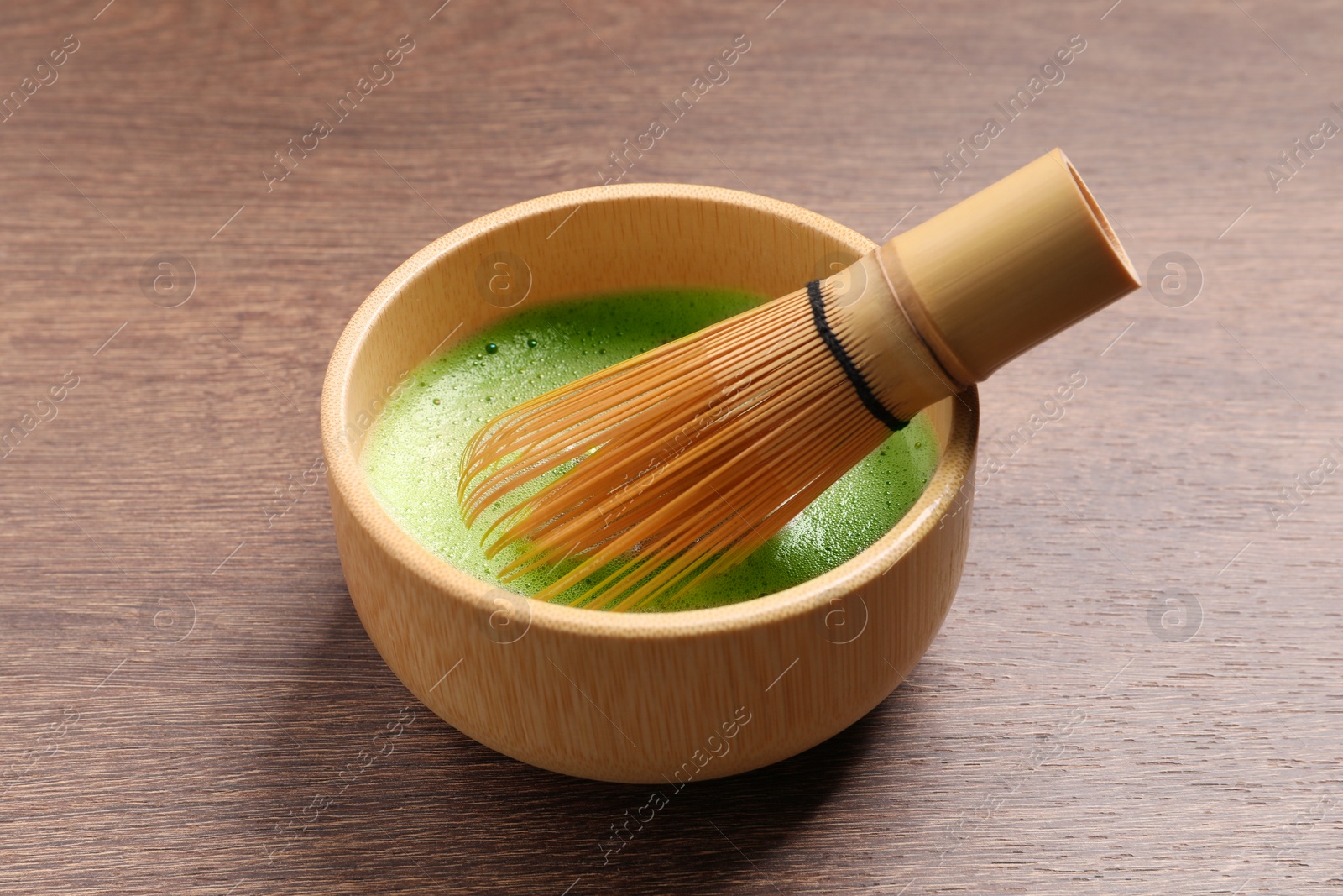 Photo of Cup of matcha tea and bamboo whisk on wooden table