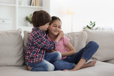 Happy brother and sister spending time together on sofa at home