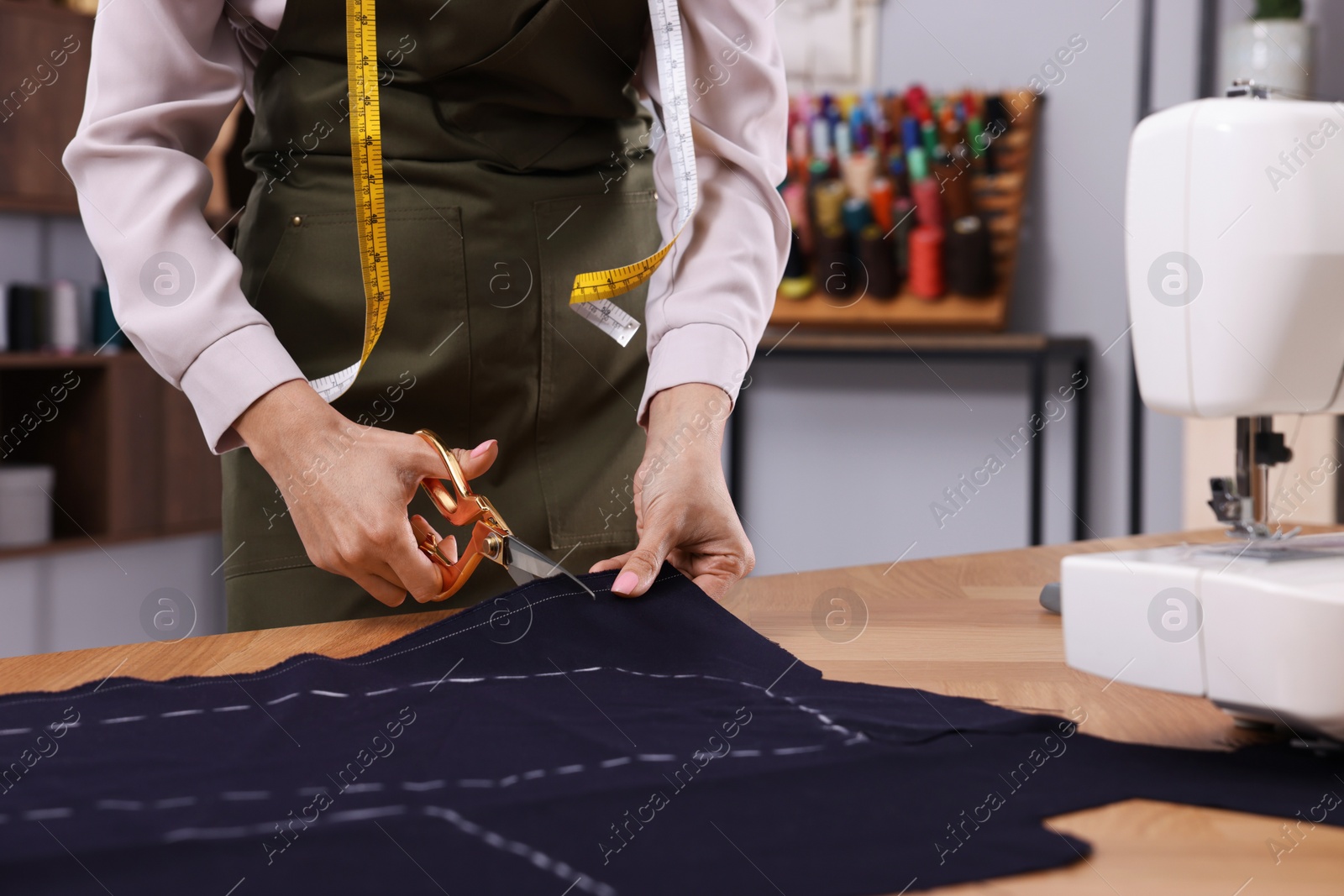 Photo of Dressmaker cutting fabric by following chalked sewing pattern in workshop, closeup