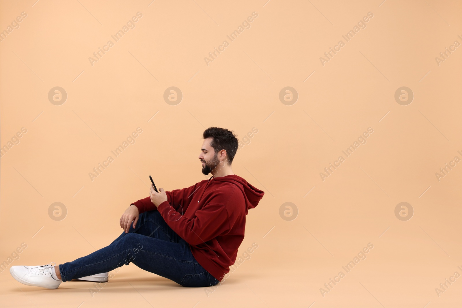 Photo of Handsome young man using smartphone on beige background, space for text