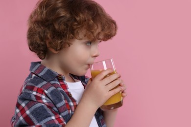 Cute little boy drinking fresh juice on pink background, space for text