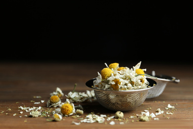 Photo of Dry chamomile flowers in infuser on wooden table, closeup