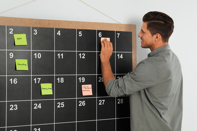 Handsome man putting sticky note on board calendar