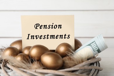 Photo of Many golden eggs, money and card with phrase Pension Investments against white wooden wall