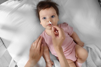 Photo of Mother cleaning nose of her baby with cotton bud on bed, top view