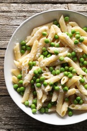 Photo of Delicious pasta with green peas and cheese in bowl on wooden table, top view